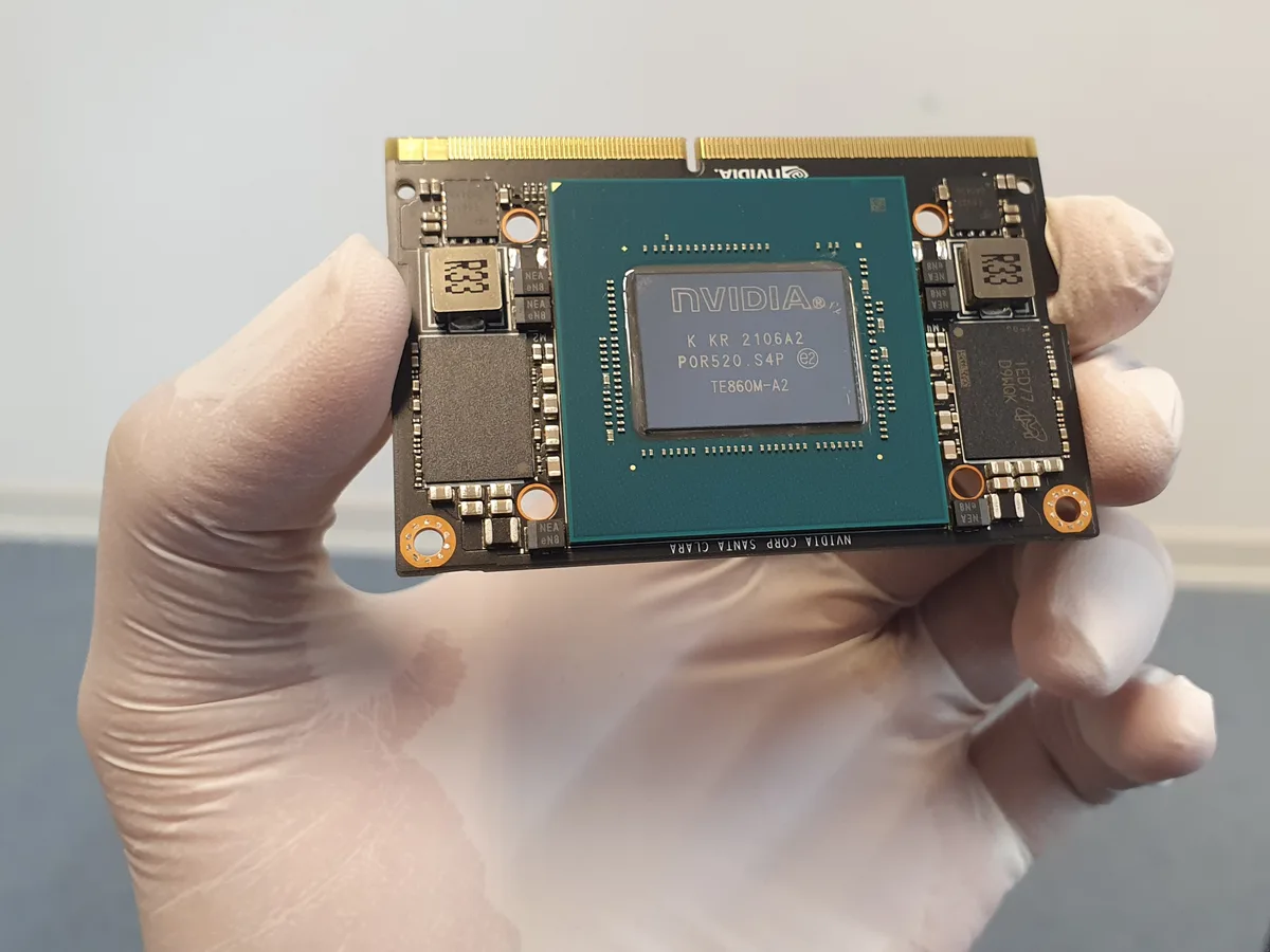 A gloved hand holding an NVIDIA Jetson compute module.
