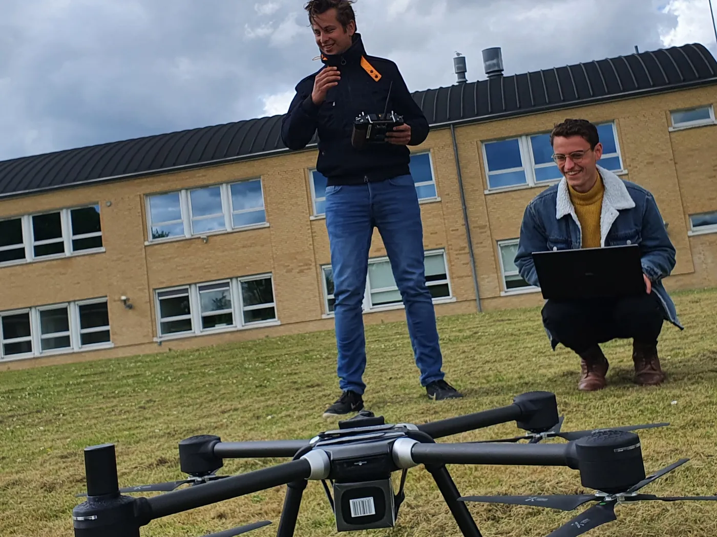 Two engineers flight-testing a hexacopter on a grass field, one at the transmitter and one crouched at a laptop.